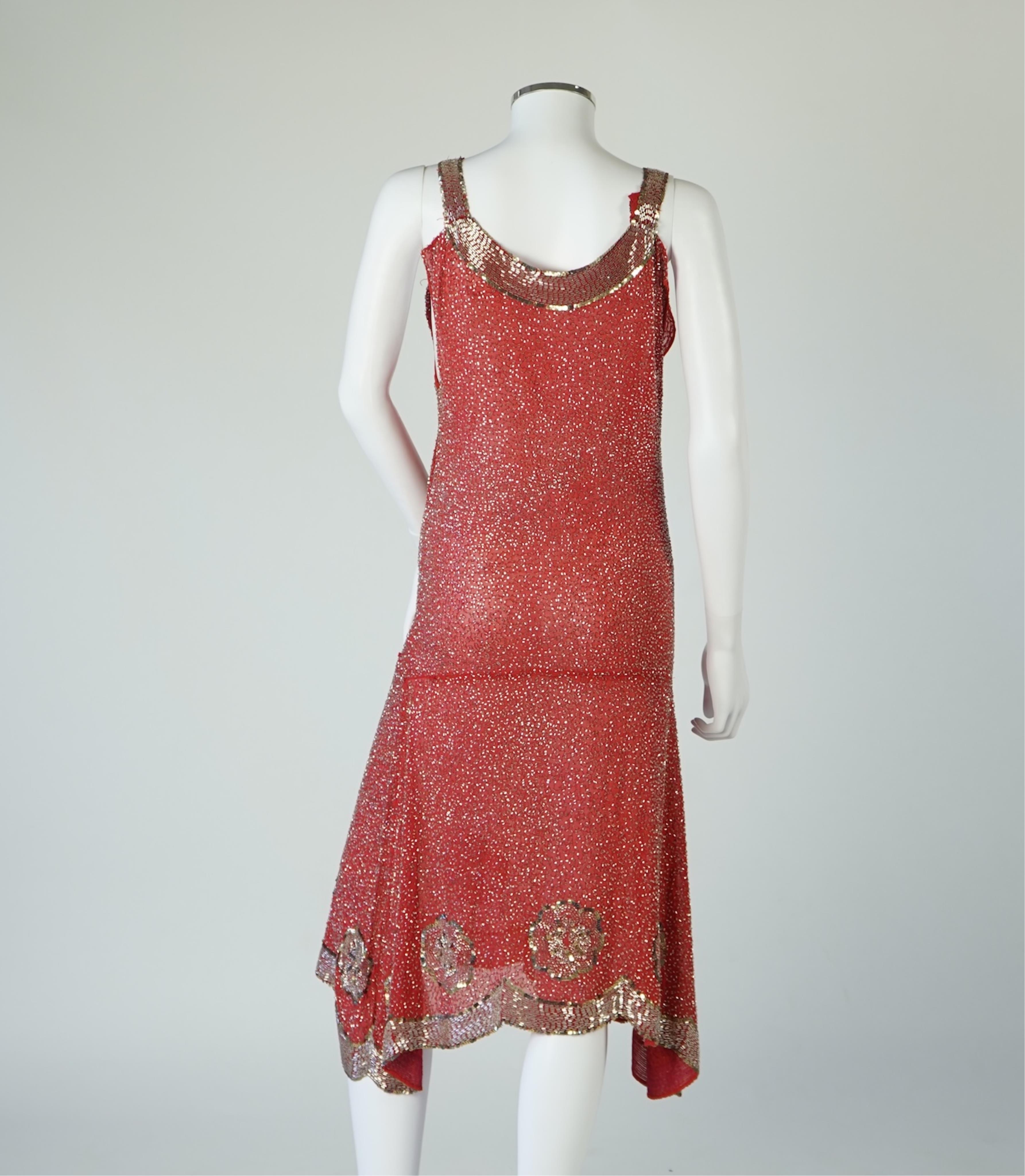 A 1920's red georgette beaded evening dress. Hand beaded and sequinned in white and gold, designed with a dropped waist, handkerchief points and wide beaded border with large stylistic floral motifs. Length 115cm. Condit